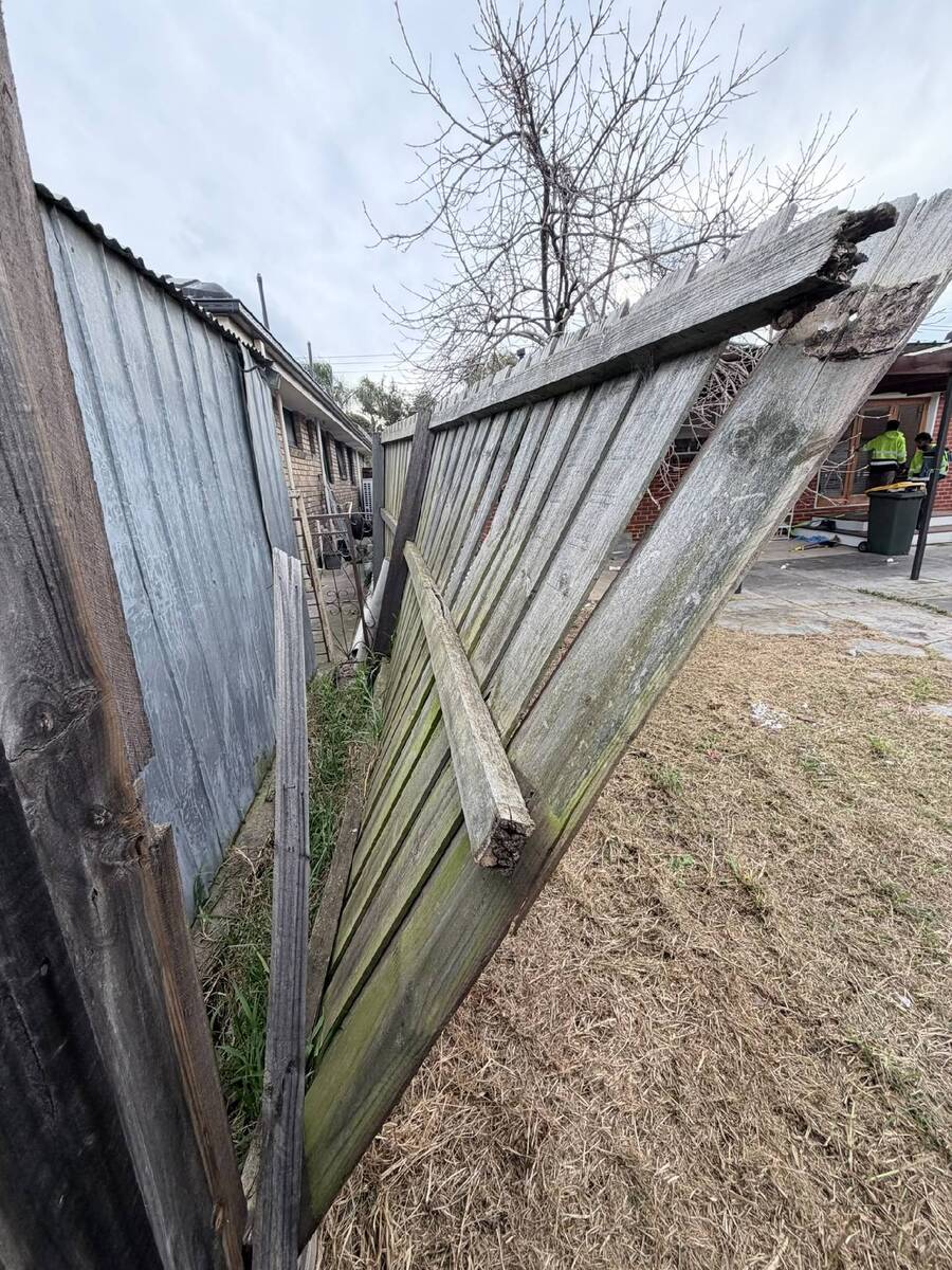 A weathered wood fence panel leaning badly after its posts failed — the classic leaning fence repair